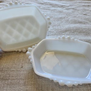 Könnte beinhalten: Zwei weiße Milchglas-Schalen mit einem perlenbesetzten Rand. Die Schalen sind achteckig und haben eine glatte, glänzende Oberfläche.