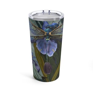 Peut inclure: Un gobelet en acier inoxydable avec un motif coloré représentant une libellule aux ailes bleues et une fleur violette. L'arrière-plan est un dégradé de vert et de bleu.