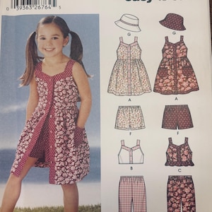 Può includere: Cartamodello Simplicity 5540, taglia A 3,4,5,6,7,8, con disegni per un vestito con bottoni frontali, pantaloncini, top e pantaloni. Le illustrazioni del cartamodello mostrano opzioni di tessuti floreali e a pois, insieme a un cappello da pescatore, offrendo varie combinazioni di capi per bambini.