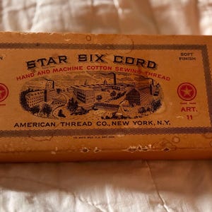 Puede incluir: Caja de hilo de coser de algodón Star Six Cord vintage. La caja es de color marrón claro con el texto "Star Six Cord Hand and Machine Cotton Sewing Thread". Presenta una ilustración y es de American Thread Co., New York, N.Y.