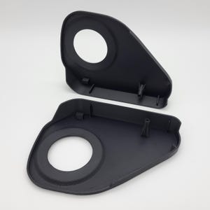 May include: Two black plastic components, possibly parts of a larger assembly, are displayed against a white background. Each piece has a rounded rectangular shape with a large circular opening and several small protrusions.