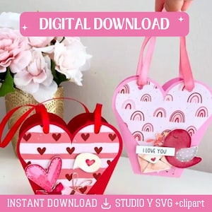 Könnte beinhalten: Zwei herzförmige Boxen mit unterschiedlichen Mustern. Eine Box ist rosa mit Regenbogen-Designs und die andere ist rot mit weißen Streifen und Herzen. Beide Boxen haben einen Griff und sind mit Valentinstag-Motiven verziert. Der Text "Ich liebe dich" ist auf der rosa Box sichtbar.