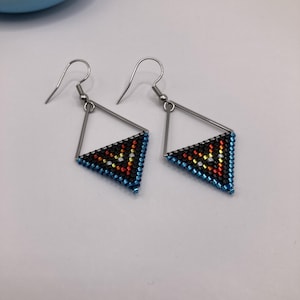 May include: A pair of beaded earrings with a geometric design. The earrings feature a triangular shape with a black background and a pattern of red, yellow, and blue beads. The edges are outlined in blue beads, and the earrings have silver-colored hooks.