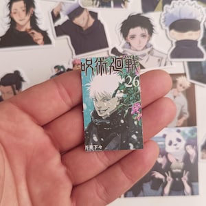 Könnte beinhalten: Ein kleiner Aufkleber mit einer Manga-Illustration eines Charakters mit weißen Haaren und schwarzer Kleidung. Der Aufkleber hat japanischen Text und die Nummer 26. Andere Anime-Charakter-Aufkleber umgeben den Aufkleber.