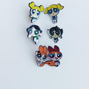 Könnte beinhalten: Sechs farbenfrohe Cartoon-Charakter-Anhänger, die jeweils ein anderes Powerpuff Girl darstellen. Die Anhänger zeigen die Charaktere Blossom, Bubbles und Buttercup mit ihren charakteristischen Frisuren und Outfits. Die Anhänger sind vor einem weißen Hintergrund angeordnet.