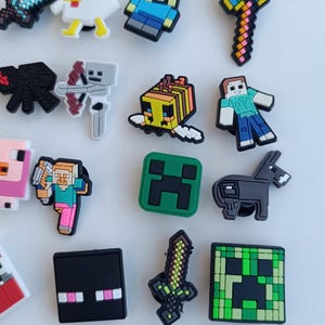 May include: A selection of colourful, pixelated character charms, including a sword, a duck, a person, a bee, a creeper, and a donkey. The charms are in various colours, such as blue, green, yellow, and black.