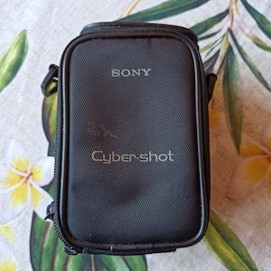 Könnte beinhalten: Schwarze Kameratasche mit Reißverschluss und dem Aufdruck "SONY Cyber-shot" auf der Vorderseite.