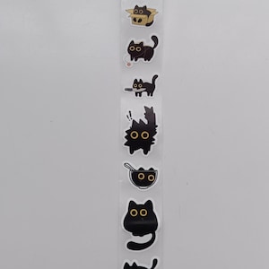 Op de afbeelding: Een strook zwarte kattenstickers met witte randen. De stickers bevatten verschillende kattenontwerpen, waaronder katten in dozen, met garen en in kommen. De katten hebben verschillende poses en uitdrukkingen, met grote, ronde ogen.