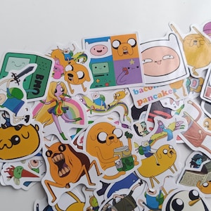 Puede incluir: Una colección de pegatinas coloridas de Adventure Time con varios personajes y diseños. Las pegatinas incluyen imágenes de Finn, Jake, BMO y otros personajes de la serie animada. Las pegatinas están sobre un fondo blanco.