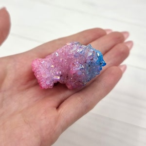 May include: A cluster of iridescent pink and blue quartz crystals. The crystals are clustered together in a natural formation, with a smooth, polished surface.