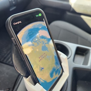 May include: A white phone holder with a black wireless charging pad, holding a smartphone with a map of North America on the screen. The phone is charging and the battery is at 73%.