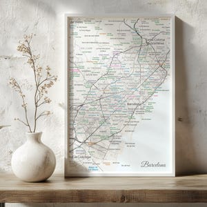 May include: A framed vertical map print of Barcelona featuring a detailed street grid, neighborhood names, and various landmarks in black text on a light background, with the word Barcelona printed in a script font in the bottom right corner.