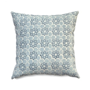 May include: Square decorative pillow with a repeating floral pattern in shades of blue and white. The pattern features stylized eight-petal flowers within a grid, creating a geometric design. The pillow has a soft, textured appearance, suitable for home decor.