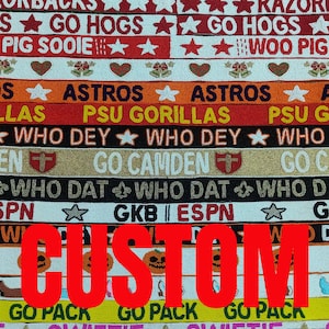 May include: A colorful, beaded fabric with various team names and phrases, including "Razorbacks," "Astros," and "Who Dey." The word "CUSTOM" is prominently displayed in red across the center of the fabric. The fabric features stars, hearts, and pumpkin designs.