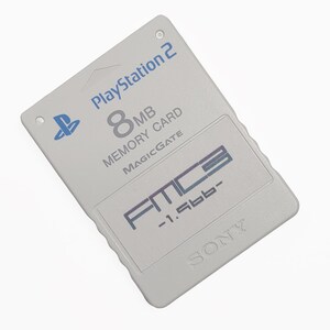 May include: A light gray PlayStation 2 8MB Memory Card with the PlayStation logo and the text "MAGICGATE". The card also features the text "FMC3 -1.56b-" and the Sony logo.