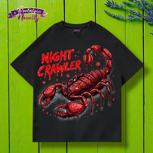 May include: Black t-shirt featuring a red scorpion graphic with the text "NIGHT CRAWLER" in a bold, stylized font. The scorpion design is detailed with a textured appearance. The shirt has a classic crew neck.