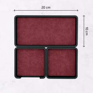 Puede incluir: Una bandeja negra con tres compartimentos, cada uno forrado con una tela color burdeos. La bandeja mide 20 cm por 10 cm.