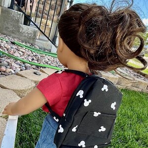 May include: A black backpack with white Mickey Mouse silhouettes all over it. The backpack has a small pocket on the front.