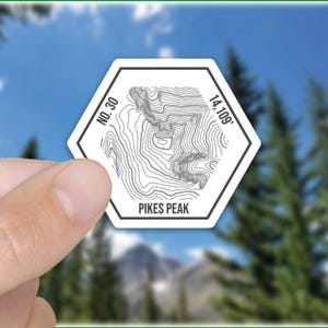 May include: White hexagonal sticker with a topographic map of Pikes Peak, Colorado. The sticker includes the text "No. 30" and "14,109'" and the words "Pikes Peak".