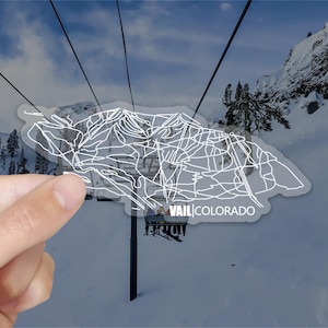 May include: A white sticker with a line drawing of the Vail, Colorado ski resort map. The sticker is on a snowy mountain background with a ski lift in the foreground. The text "Vail Colorado" is printed on the sticker.