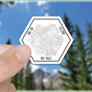 May include: White hexagonal sticker with a topographic map design of Mt. Yale, a 14,200 foot peak. The sticker also includes the text "No. 20" and "Mt. Yale".