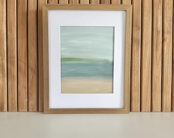 May include: A framed abstract landscape painting with a light wood frame. The artwork features a serene scene with a light blue sky, a green horizon line, and a sandy beige foreground. The painting is displayed against a wooden slatted wall.