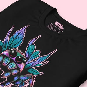 May include: Black t-shirt with a colorful graphic of a spider with wings. The spider has iridescent blue, green, and purple colors. The text "Little Spoons" is on the tag.