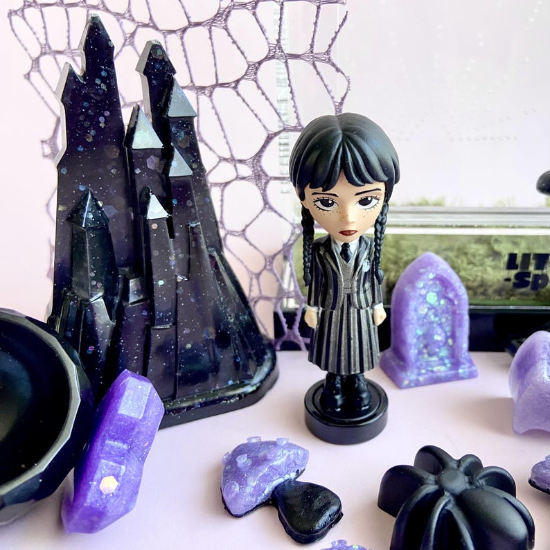 Close-up of handmade gothic castle décor and Wednesday Addams figure for jumping spider enclosure.