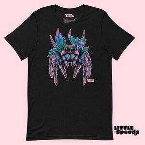 May include: Black t-shirt with a colorful jumping spider graphic. The spider has blue, purple, and green accents and is surrounded by pink and green leaves. The text "LITTLE SPOODS" is printed on the shirt.