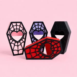 Multiple color options of the magnetic jumping spider coffin hide displayed together on a pastel pink background.
