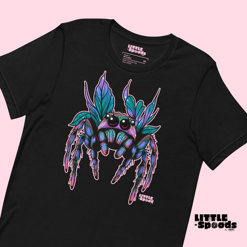 May include: Black t-shirt with a colorful illustration of a jumping spider with wings. The spider has large, iridescent eyes and is surrounded by pink and blue foliage. The text "LITTLE SPOODS" is printed on the shirt.