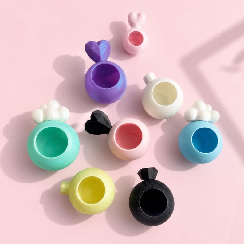 Jumping spider hides in multiple colors, sizes, and magnet styles on pastel pink background, including jumping spider heart hide and cloud hide. Colors are pastel pink, glitter purple, green, white, blue, yellow and black. For juvenile and adult spiders.