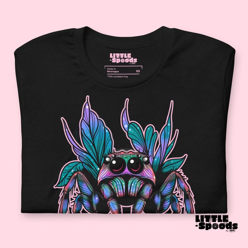 May include: Black t-shirt with a colorful illustration of a jumping spider with iridescent wings. The spider has large, round eyes and is surrounded by a floral design. The shirt has the text "LITTLE -SPOODS" on the front.