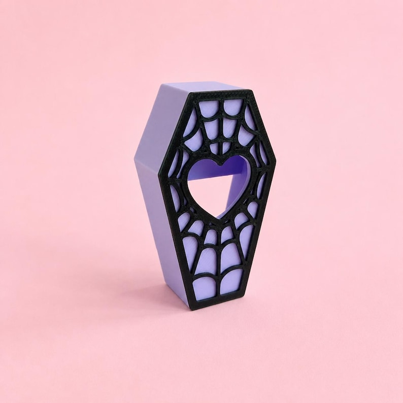 Purple magnetic jumping spider coffin hide with black spiderweb design on a pastel pink background.
