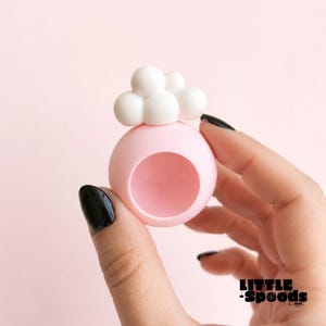 Hand holding a pastel pink magnetic jumping spider hide with a white cloud magnet topper in a pastel pink background
