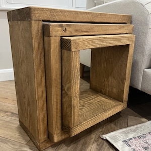 May include: A set of three wooden nesting tables with a natural brown finish. The tables are made of solid wood and have a simple, rustic design.