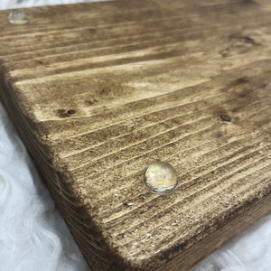 May include: A close-up of a wooden serving tray with a dark brown stain. The tray has two clear rubber feet on the bottom.