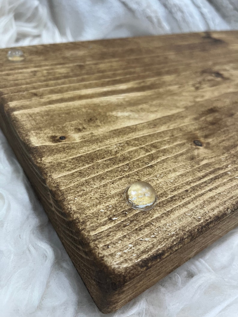 May include: A close-up of a wooden serving tray with a dark brown stain. The tray has two clear rubber feet on the bottom.