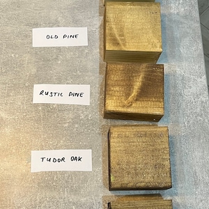 May include: Five wood samples stained in different colors: clear, old pine, rustic pine, tudor oak, and jacobean. The samples are arranged vertically from top to bottom.