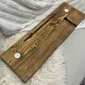 May include: A wooden bath tray with two small white candle holders. The tray is stained a dark brown color and has a groove in the center for holding a glass of wine or a book.