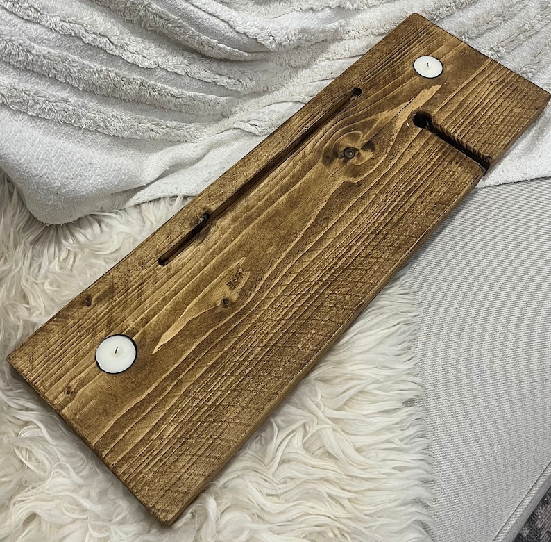 May include: A wooden bath tray with two small white candle holders. The tray is stained a dark brown color and has a groove in the center for holding a glass of wine or a book.