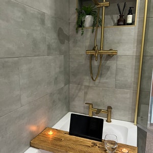 May include: A wooden bath tray with a built-in phone or tablet holder, a glass of water, and two candles. The tray is placed on a white bathtub.