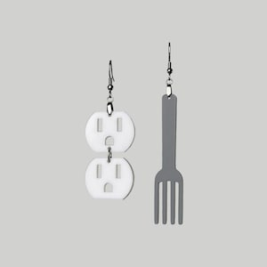 May include: A pair of earrings, one featuring a white double outlet design and the other a gray fork design.