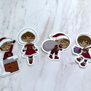 Puede incluir: Cuatro pegatinas navideñas con personajes de dibujos animados con gorros de Papá Noel y trajes rojos. Un personaje está en una chimenea, otro sostiene un regalo y un tercero lleva un saco. Las pegatinas tienen bordes blancos.