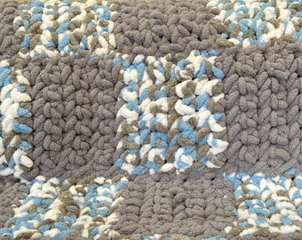 Könnte beinhalten: Eine dicke Strickdecke in Grau, Weiß und Blau. Die Decke ist aus dickem Garn gefertigt und hat eine weiche, strukturierte Oberfläche.