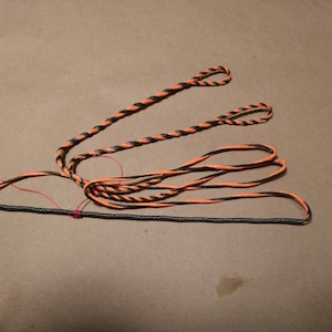 May include: A black and orange bowstring for archery. The string is made of a braided material and has a red thread running through it.
