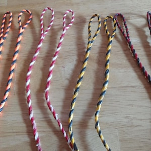 May include: Six different colored bowstrings for archery. The bowstrings are made of a braided material and have a loop at each end. The colors are orange and black, red and white, yellow and black, black and red, and black and blue.