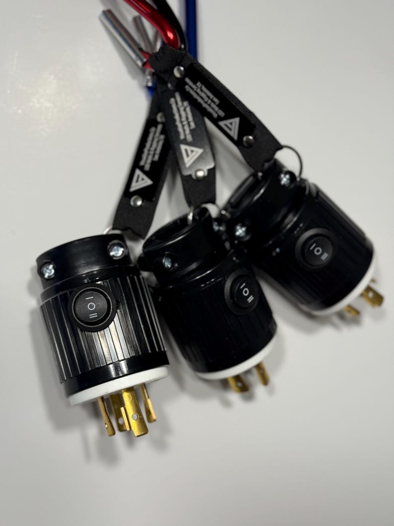 May include: Three black electrical plugs with white and gold prongs are hanging from a carabiner. Each plug has a black on/off switch and is attached to a black strap with white text and a triangle logo.