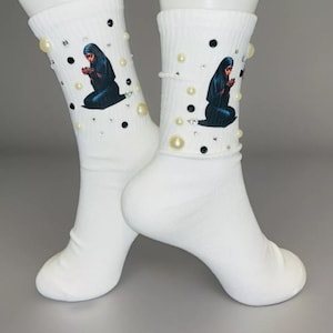 May include: White socks with a black and white image of a woman wearing a headscarf. The socks are decorated with white pearls and black rhinestones.