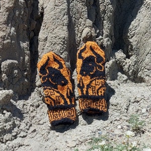 Könnte beinhalten: Ein Paar orange-schwarze Fingerlose Strickhandschuhe mit geometrischem Muster. Die Handschuhe zeigen eine schwarze Silhouette eines Stierkopfes.